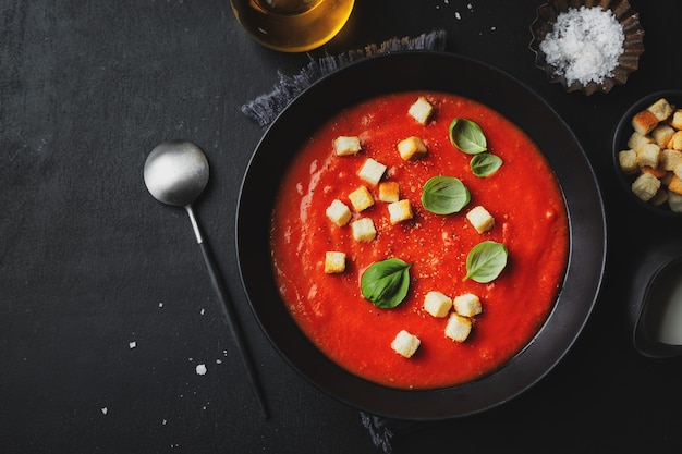 Sopa de tomate sabrosa cremosa servida en un tazón sobre fondo oscuro. Vista desde arriba.