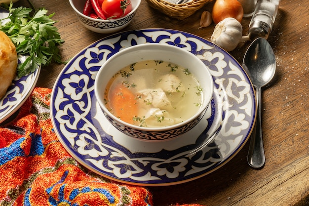 Sopa Tovuk Shurpa. Caldo de pechuga de pollo con fideos caseros y zanahorias en un plato con adornos tradicionales de Uzbekistán