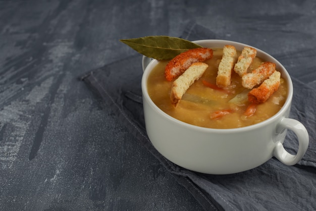 Foto sopa tradicional de guisantes amarillos con platos duros en plato blanco con asas. sopa vegetariana sobre fondo gris con espacio de copia.