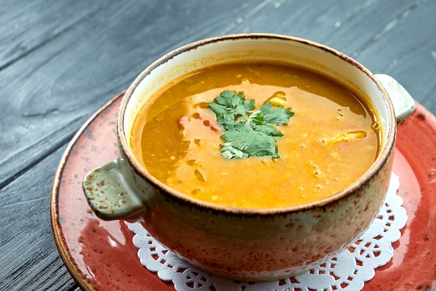 Sopa tradicional marroquí - Harira, sopa de lentejas amarillas con cilantro en una placa roja sobre una superficie de madera negra. Sopa de dieta