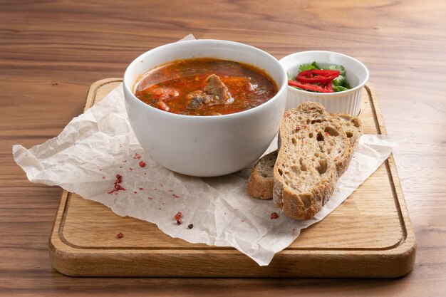 Sopa tradicional ucraniana hecha de remolacha, verduras y carne con pan sobre una mesa de madera.