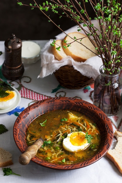 Sopa verde primavera com ervas, legumes e ervilhas, servido com ovo e creme de leite. Estilo rústico.