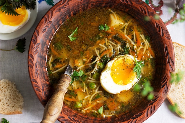 Sopa verde primavera com ervas, legumes e ervilhas, servido com ovo e creme de leite. Estilo rústico.