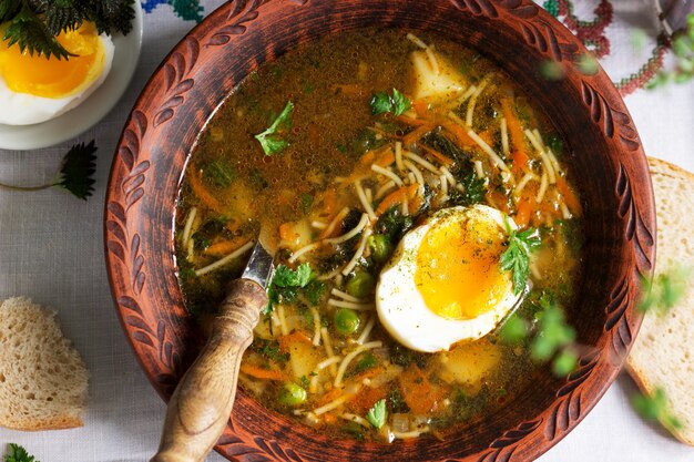 Sopa verde de primavera con hierbas, verduras y guisantes verdes, servida con huevo y crema agria. Estilo rústico