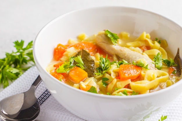 Sopa y verduras de fideos del pollo en un cuenco blanco en un fondo blanco, espacio de la copia.