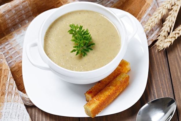 Sopa de verduras con perejil y pan frito en una mesa de madera.