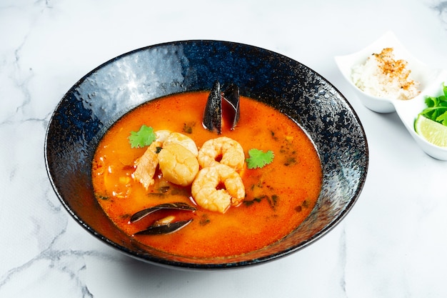 Sopa vietnamita de Tom Yum com frutos do mar. Sopa vermelha com camarão, vieiras, mexilhões, salmão em uma tigela escura e elegante sobre uma mesa de mármore.