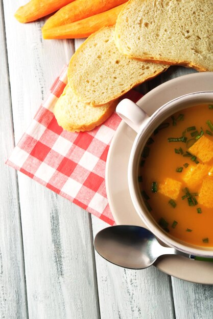 Sopa de zanahoria con crema y cuchara sobre fondo de madera de color