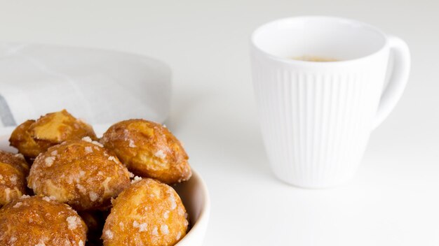 Soplos de chouquettes franceses con perles de azúcar en plato con taza de café blanco pasta choux clásica ...