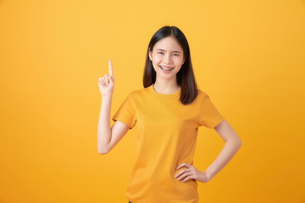 El soporte asiático sonriente del adolescente y señalar con el dedo en naranja.