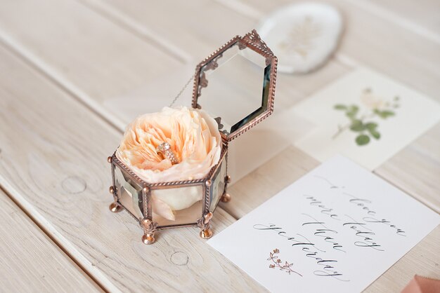 Foto soporte de ataúd cuadrado vintage de decoración de boda con peonía rosa dentro y tarjeta de invitación de anillo de bodas.