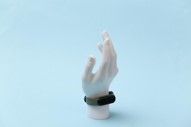 Soporte de mano maniquí blanco con pulsera inteligente sobre fondo azul. Gadgets modernos