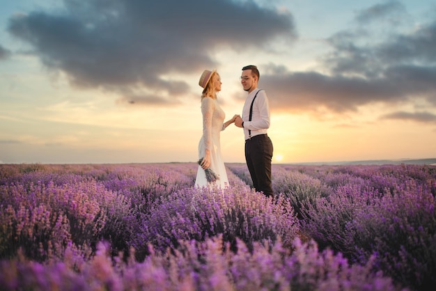 Soporte de recién casados felices en campo floreciente de lavanda al amanecer.