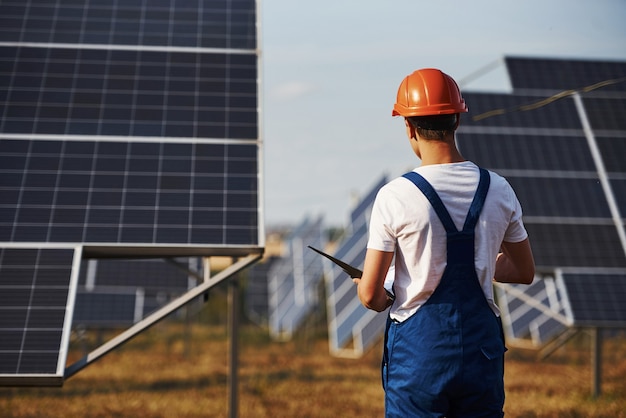 Soportes con bloc de notas. Trabajador de sexo masculino en uniforme azul al aire libre con baterías solares en un día soleado.