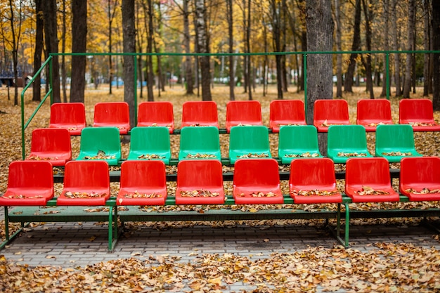 Soportes deportivos vacíos con asientos rojos y verdes en un día de otoño.