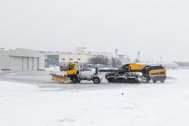 Sopradores de neve do aeródromo limpando a área perto do hangar de aviões no aeroporto durante uma forte nevasca