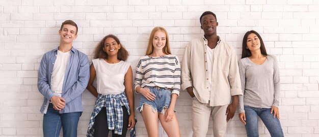 Sorgefreie Gruppe internationaler Studenten-Hipster, die über einer weißen Wand posieren, Jugendkultur-Konzept