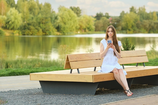 Sorglose Frau liest Nachricht auf Smartphone, während sie auf Bank im Stadtpark sitzt