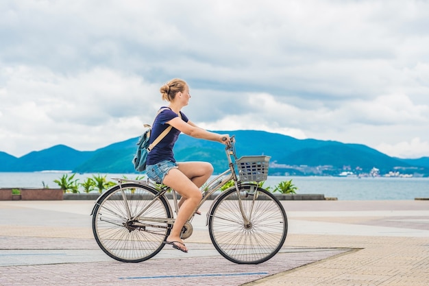 Sorglose Frau mit dem Fahrrad, das durch das Meer reitet, das Spaß hat und lächelt.