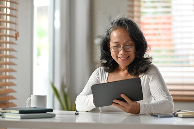 Sorglose Frau mittleren Alters liest Nachrichten online und überprüft soziale Medien auf einem digitalen Tablet Älteres Technologiekonzept