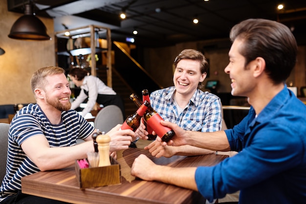 Sorglose Freunde klirren Bierflaschen im Café