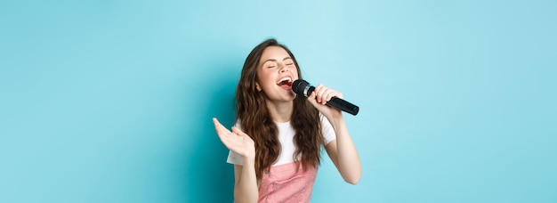 Sorglose schöne Frau führt Lieder auf, die im Mikrofon mit Leidenschaft singen und Karaoke im Stehen spielen