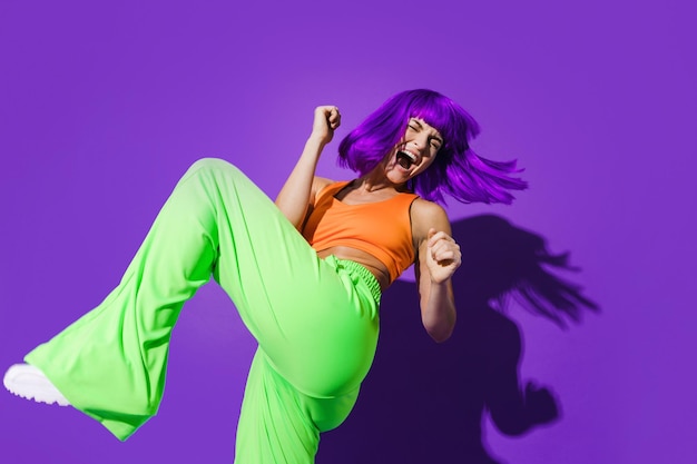 Sorglose Tänzerin in farbenfroher Sportkleidung, die sich vor violettem Hintergrund amüsiert
