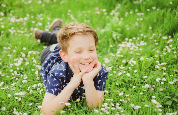 Sorgloser lächelnder Junge, der auf Blumenfeld liegt. Nettes Kind, das auf Rasen genießt und träumt.