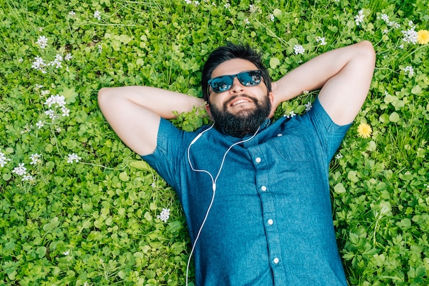 Sorgloser Mann, der auf dem Gras und der hörenden Musik liegt