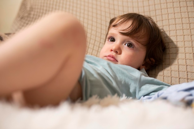 Sorgloses eineinhalbjähriges Baby, das zu Hause auf der Couch ruht und aufmerksam aussieht