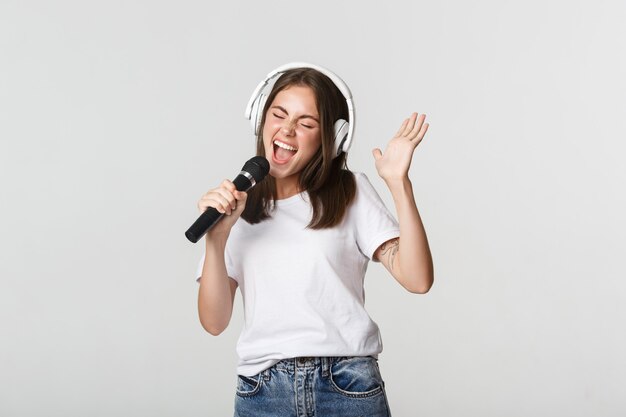 Sorgloses lächelndes Mädchen, das Karaoke spielt und im Mikrofon mit Kopfhörern singt.