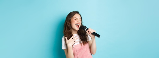 Sorgloses schönes Mädchen singt Lieder im Mikrofon mit Leidenschaft und spielt Karaoke im Stehen