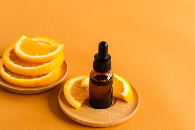 Soro com vitamina C, um frasco de óleo essencial de laranja e fatias de frutas frescas em um fundo laranja.