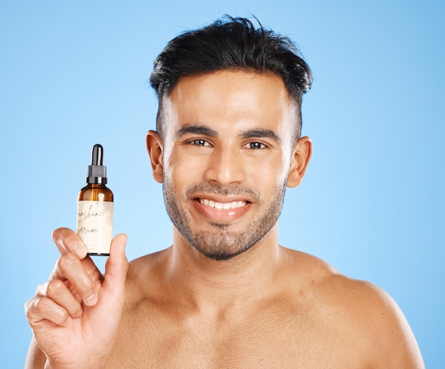 Foto soro de homem indiano e cuidados com a pele com sorriso para beleza natural facial orgânico e bem-estar com fundo de estúdio azul cuidado corporal masculino e com óleo cosmético para brilho suave da pele e prazer em hidratar