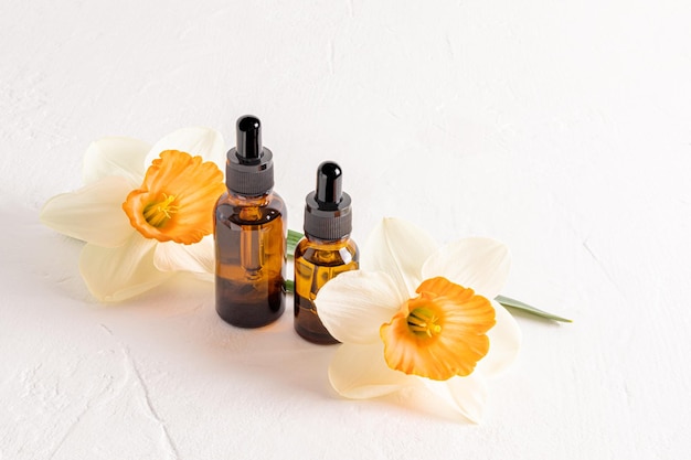 Soro facial em frascos de cosméticos de vidro com uma pipeta para cuidados diários com a pele em um fundo texturizado branco com narcisos frescos cosméticos naturais