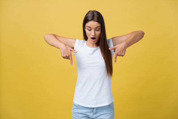 Foto sorprenda a la joven apuntando hacia un lado con el dedo mientras abre la boca sobre un fondo amarillo