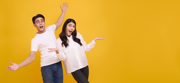 Sorprenda a la joven pareja asiática hombre y mujer felices y asombrados sobre fondo amarillo panorámico.