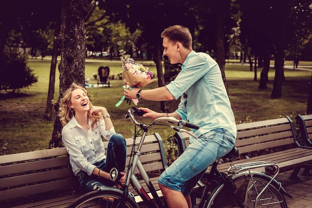 Sorprende el ramo de flores de un hombre casual en bicicleta a una linda mujer rubia.