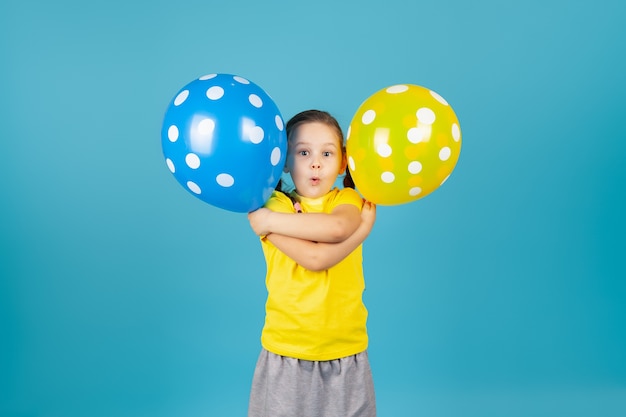 Sorprendida chica con coleta con la boca abierta en camiseta amarilla se abraza y sostiene globos