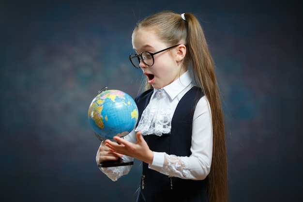 Sorprendida colegiala rubia mira el globo terráqueo