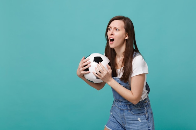 Sorprendida y decepcionada fanática del fútbol apoya al equipo favorito con un balón de fútbol mirando a un lado aislado en un fondo azul turquesa. Emociones de la gente, concepto de ocio familiar deportivo. Simulacros de espacio de copia.