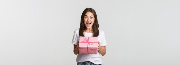 Sorprendida feliz cumpleaños niña recibiendo regalo envuelto fondo blanco.