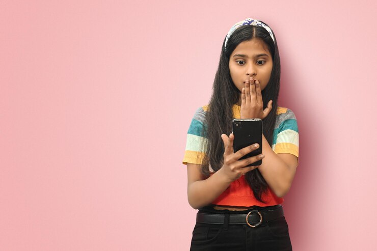 Sorprendida joven india de Asia usando un teléfono móvil de pie aislada como un lector de teléfono, verifique las noticias de los seguidores de instagram, fotos inesperadas, increíbles, maquetas, espacio de copia