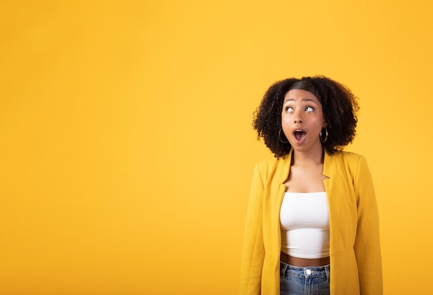 Sorprendida joven negra con la boca abierta mirando el espacio libre aislado en el fondo amarillo del estudio