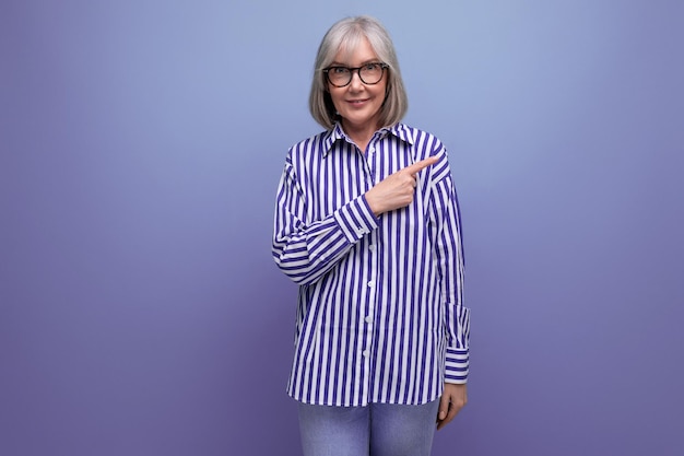 Sorprendida mujer de mediana edad con cabello gris señala con el dedo a un lado en un estudio brillante