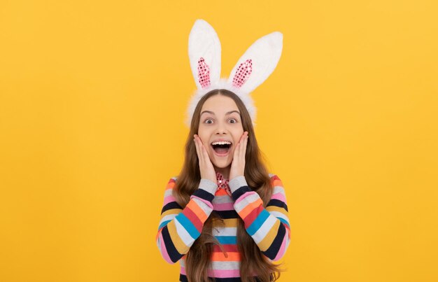 Sorprendida niña de pascua con orejas de conejo y pajarita sobre fondo amarillo