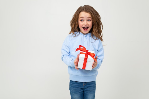 Sorprendido alegre niña feliz recibió un regalo en una pared blanca