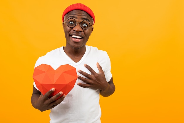 Sorprendido guapo americano en camiseta blanca tiene corazón de papel 3d para el día de San Valentín en amarillo