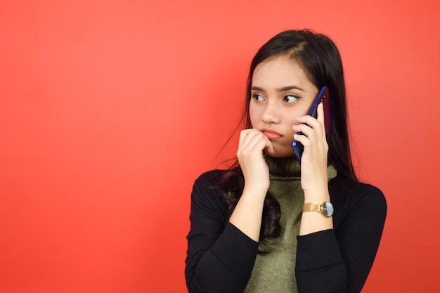 Sorprendido y hacer una llamada telefónica de una hermosa mujer asiática aislada en un fondo rojo