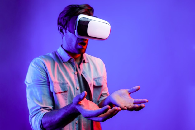 Sorprendido hombre feliz sosteniendo mientras usa gafas VR en la desviación de la luz de neón